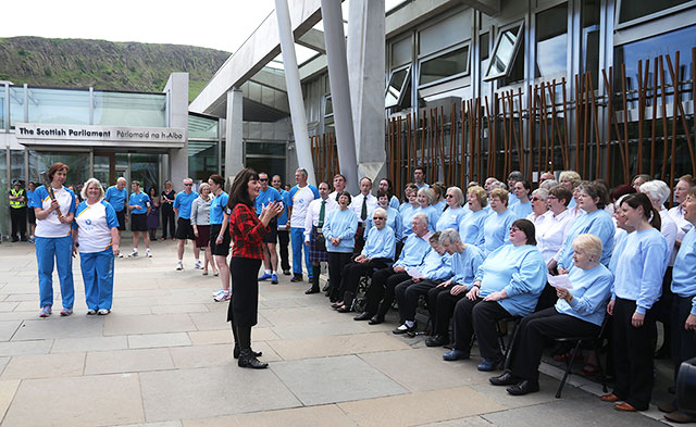 The Queen's Baton emerges from The Scottish Parliament in front of a choir singing in Gaelic