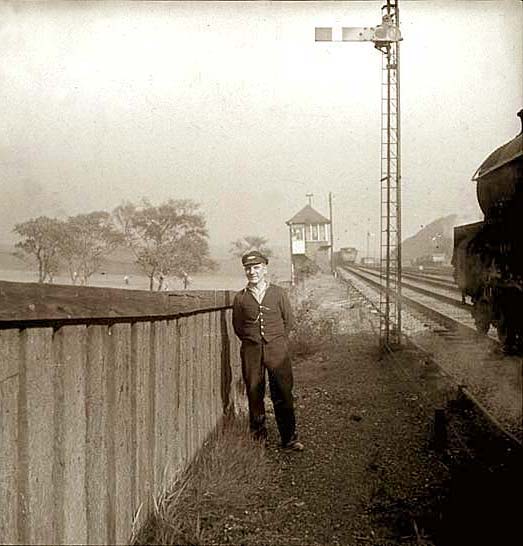A railwayman stands beside the track as an engine passes heading towards a signalbox.  Where is it?