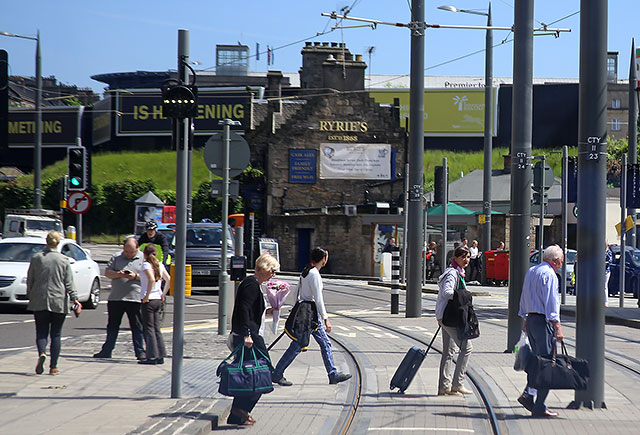 Edinburgh Tram Service  -Travellers at Haymarket, heading forHaymarket Station cross the tram lines in front of the tram  -  June 2014