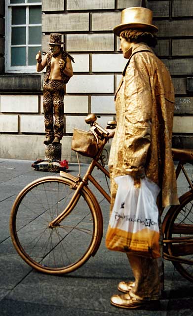 The man with the golden cycle stops to watch another street entertainer in the Edinburgh Royal Mile