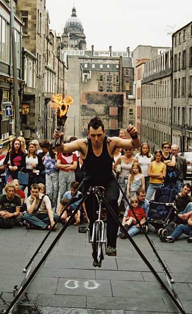 Edinburgh Festival 2003  -  A unicyclist on a tightrope is about to juggle three flaming torches